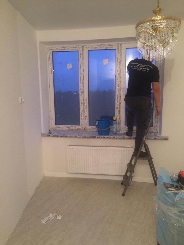 Уборщик моет окно в жилой комнате после ремонта